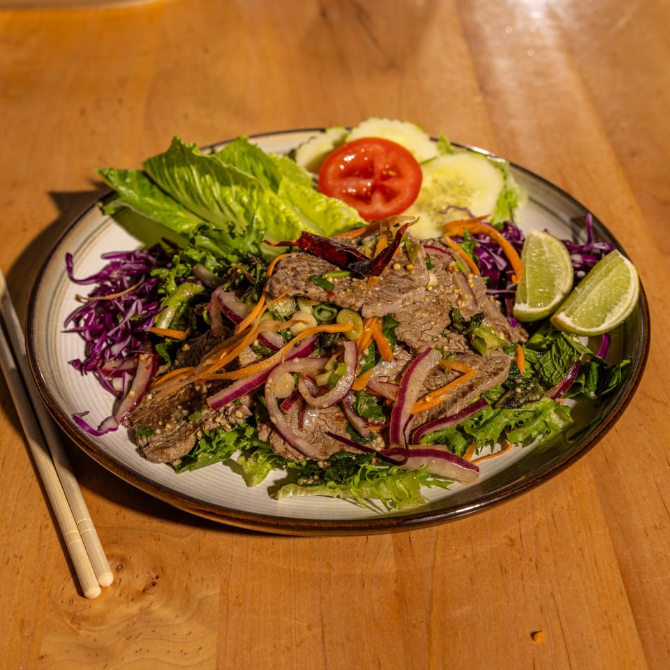 Relish Thai Cuisine's spicy beef salad with red onions, lettuce, and lime wedges.